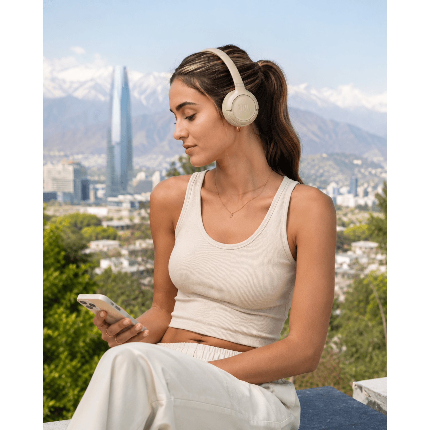 Mujer usando audífonos bluetooth JBL Tune 530BT en un paisaje urbano y montañoso.