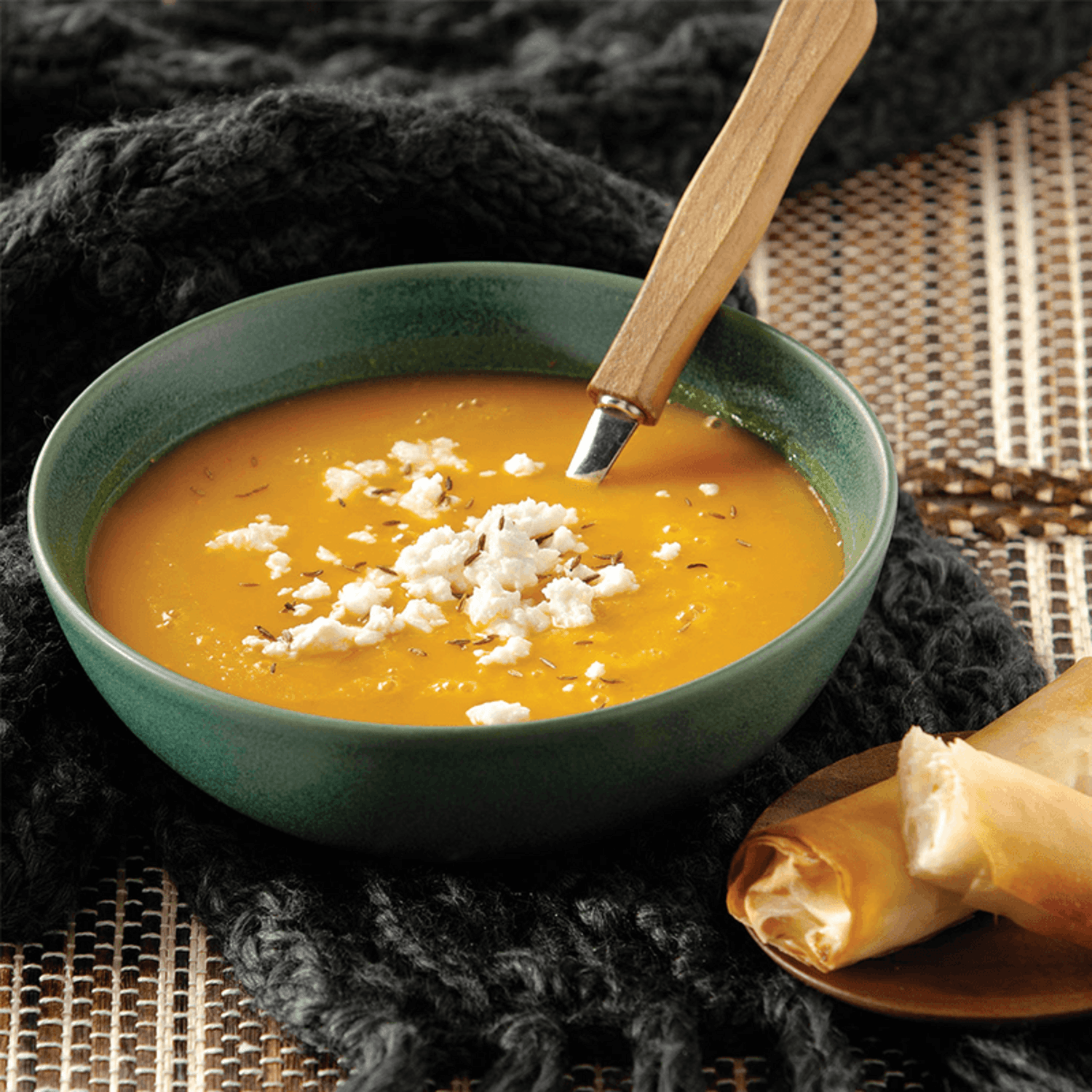 Cuenco de sopa amarilla con queso en trozos, acompañado de un rollito, preparado con la Máquina para Sopas Philips HR2203 Cremas y Compotas 1.2L.