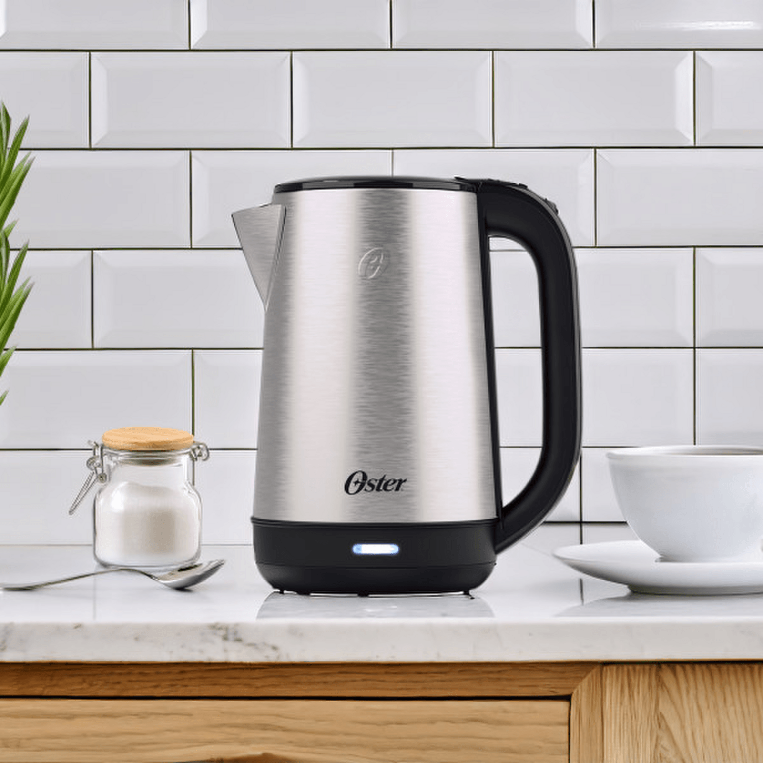 Hervidor Oster 2L 1200W Acero Inox Apagado Auto 2220516 en cocina moderna con recipiente de azúcar y taza.